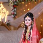 South Asian bride in traditional wedding attire with floral and gold accents indoors.